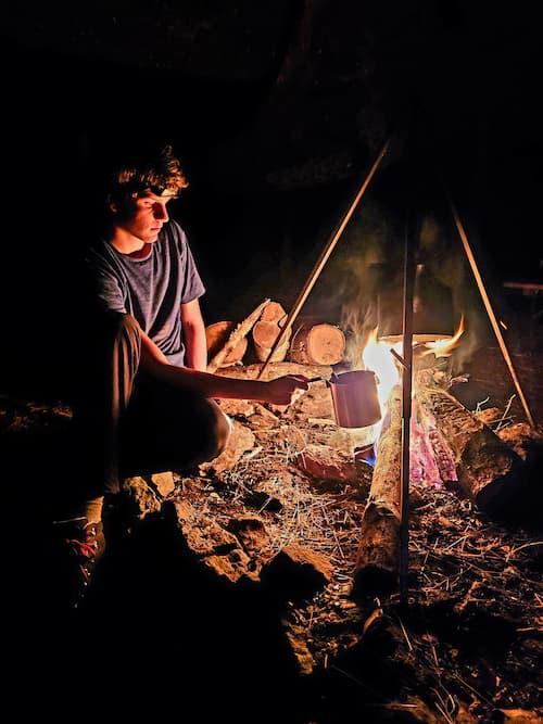 Een persoon houdt een pannetje boven een vuur