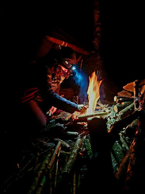Iemand maakt ’s nachts een vuur in het bos met behulp van hoofdlampen voor verlichting.