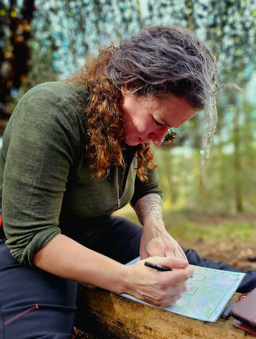 Een vrouw markeert geconcentreerd een kaart tijdens een bushcraft-navigatiesessie.